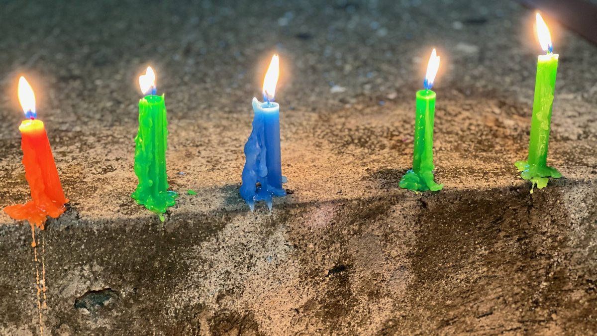 Горящие свечи оранжевого, зеленого и синего цвета стоят в ряд, с них стекает расплавленный воск